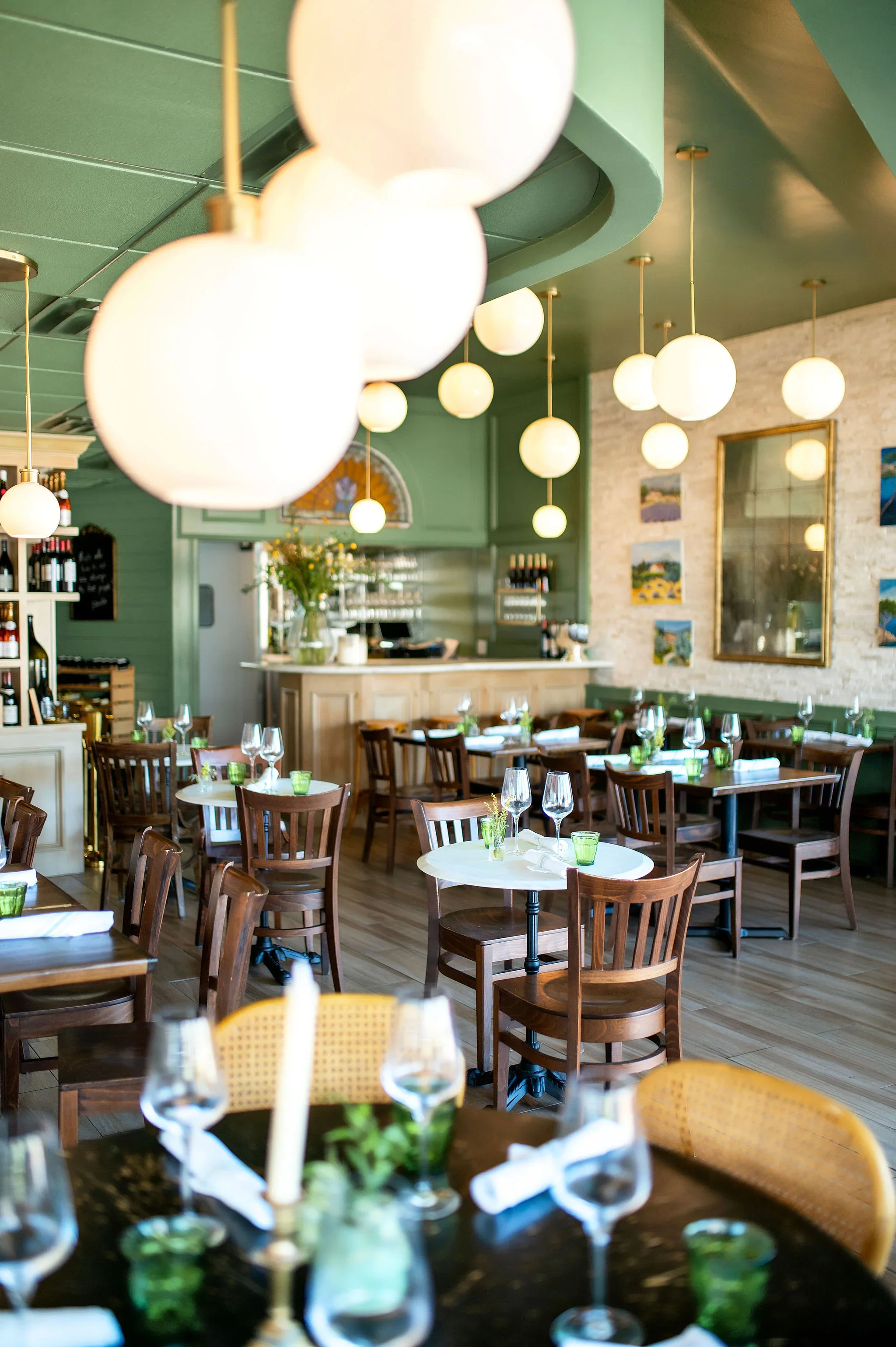 Interior of Bistro Mistral Bellaire — green walls, globe lights, and set tables