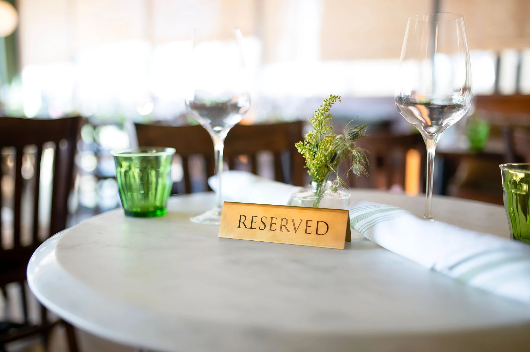 Reserved sign on a marble table at Bistro Mistral — wine glasses, fresh herbs, and green bistro glassware